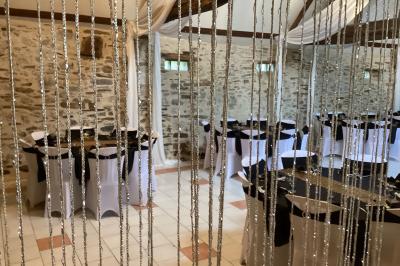 Salle à manger rustique avec table en bois dressée, mur en pierre apparente, étagères intégrées et cuisine ouverte.