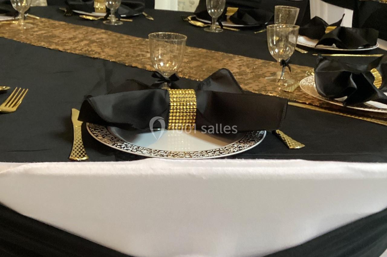 Table décorée avec une nappe noire et blanche, ornée de nœuds noirs, détails dorés et vaisselle élégante.