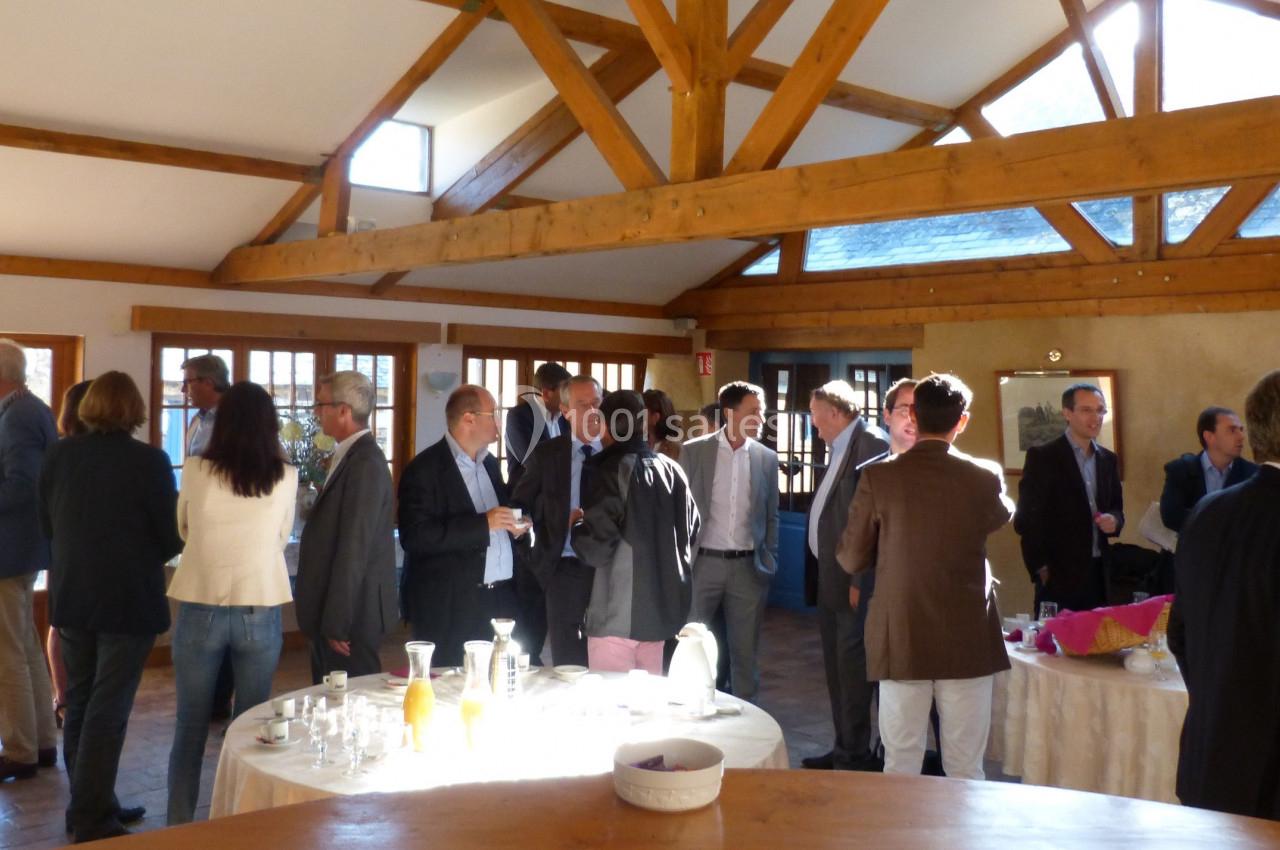 Groupe de personnes debout dans une salle lumineuse avec charpente en bois, discutant autour de tables dressées.