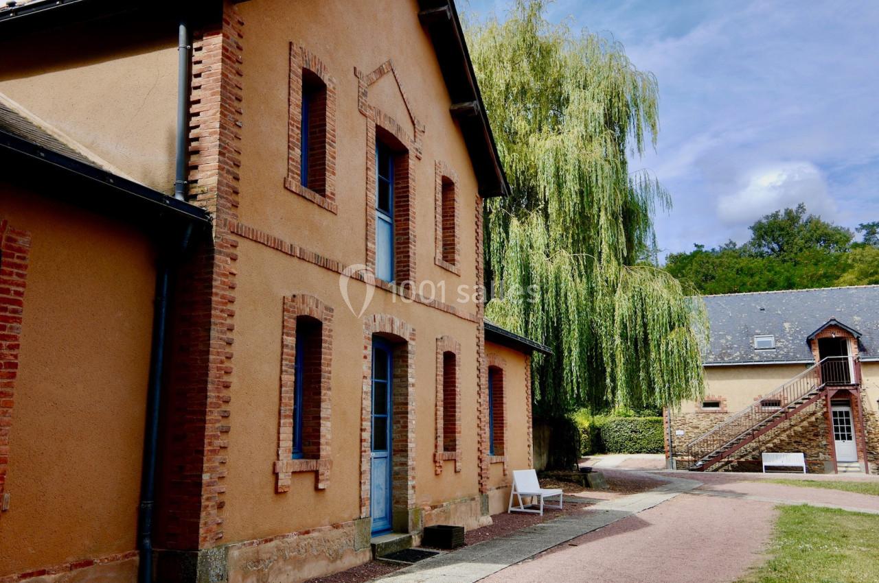 Bâtiment en briques rouges avec un saule pleureur à proximité, situé dans un environnement verdoyant.