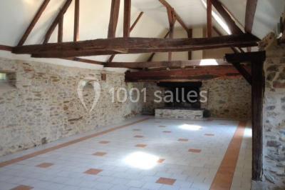 Salle à manger rustique avec table en bois dressée, mur en pierre apparente, étagères intégrées et cuisine ouverte.