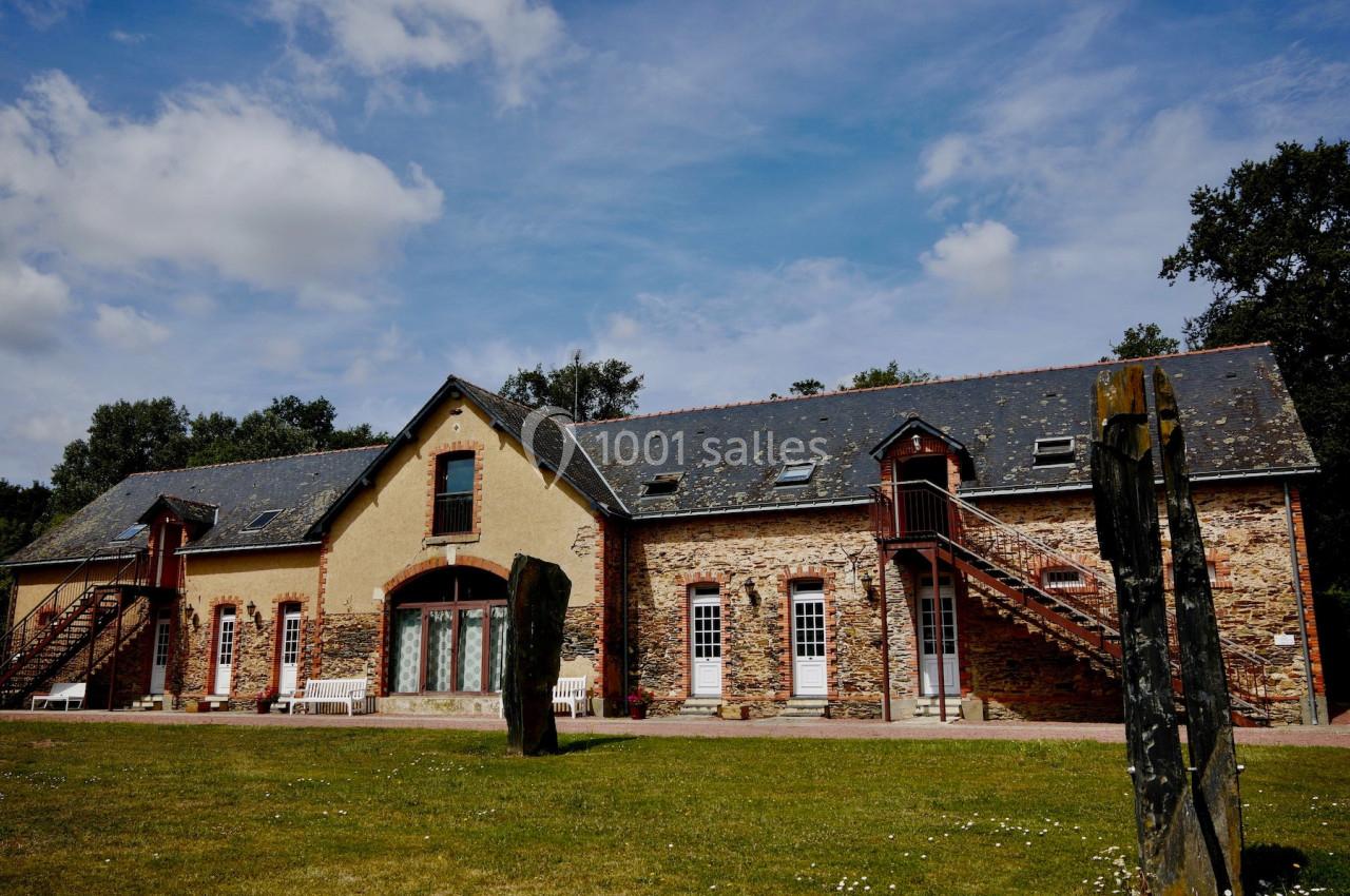 Bâtiment en pierre et crépi avec escaliers extérieurs, entouré de pelouse et d'arbres sous un ciel partiellement nuageux.