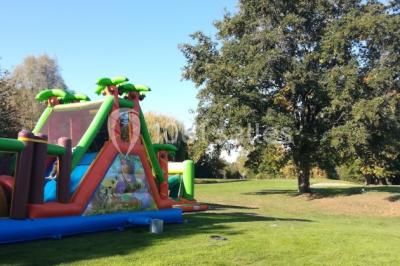 Salle à manger rustique avec table en bois dressée, mur en pierre apparente, étagères intégrées et cuisine ouverte.