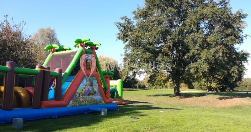 Structure gonflable colorée installée sur une pelouse verte, entourée d'arbres sous un ciel dégagé.