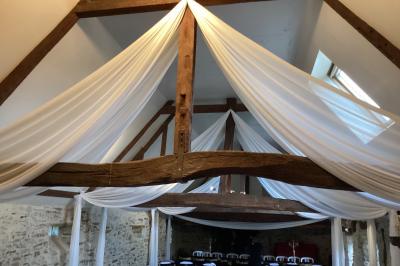 Salle à manger rustique avec table en bois dressée, mur en pierre apparente, étagères intégrées et cuisine ouverte.