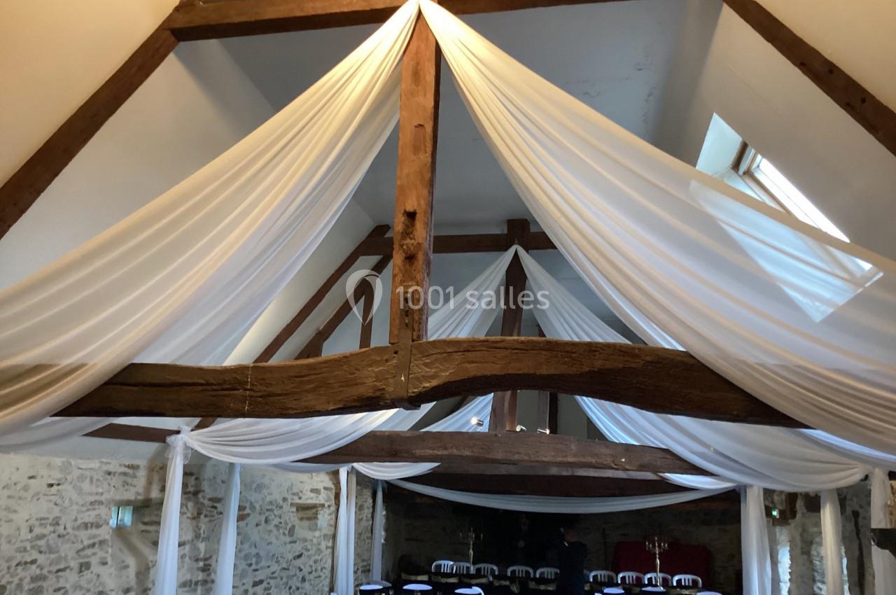 Plafond en poutres apparentes avec drapés blancs suspendus, dans une salle en pierre aménagée pour un événement.