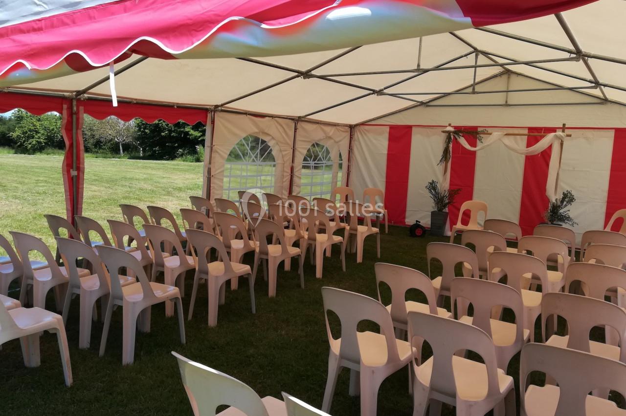 Chaises en plastique disposées sous une tente blanche et rouge installée sur une pelouse.