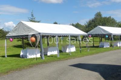 Salle à manger rustique avec table en bois dressée, mur en pierre apparente, étagères intégrées et cuisine ouverte.