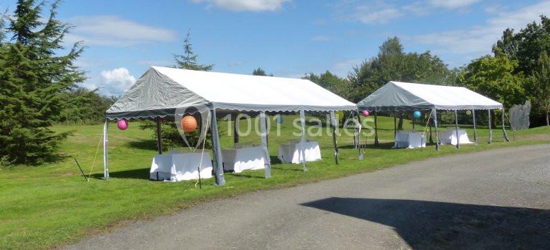 Deux tentes blanches installées sur une pelouse, décorées de lanternes colorées, avec des tables dressées dessous.