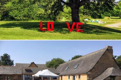 Salle à manger rustique avec table en bois dressée, mur en pierre apparente, étagères intégrées et cuisine ouverte.