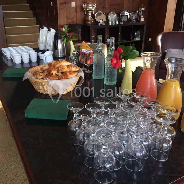 Buffet avec croissants, jus en carafes, tasses et verres disposés sur une table sombre dans un espace intérieur.