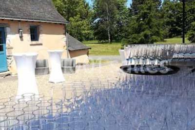 Salle à manger rustique avec table en bois dressée, mur en pierre apparente, étagères intégrées et cuisine ouverte.