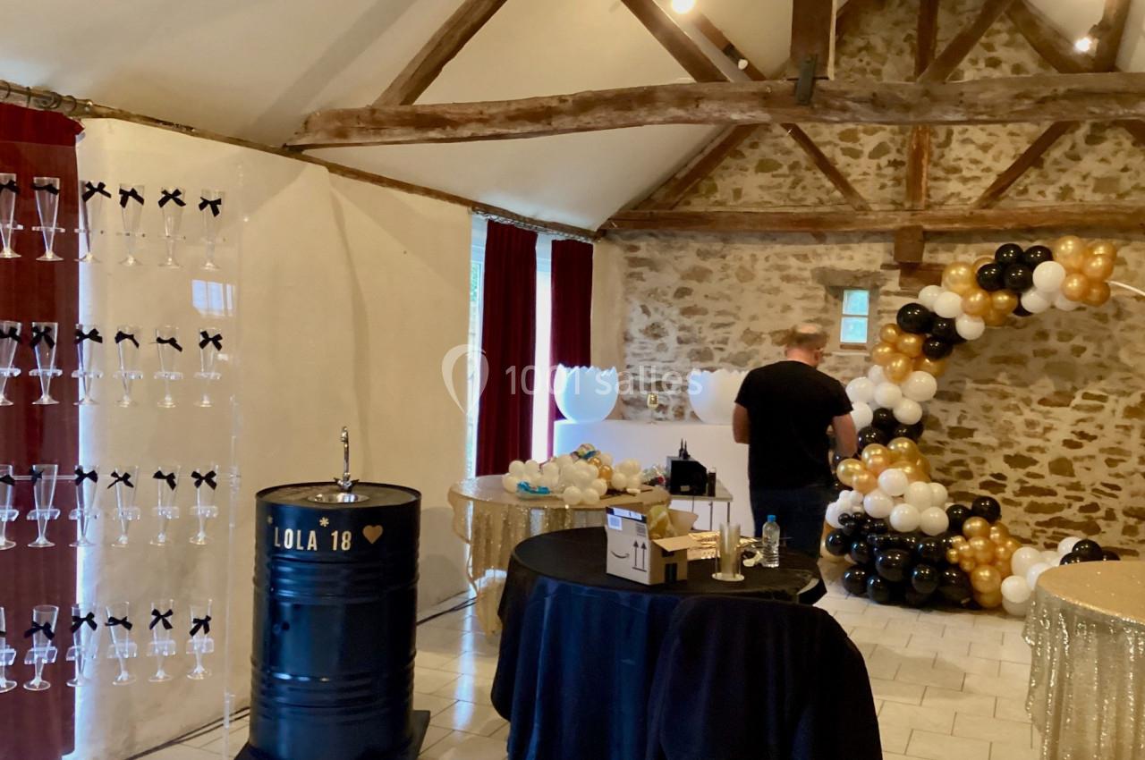 Salle décorée pour une fête avec ballons noirs, blancs et dorés, table ronde et présentoir à flûtes.