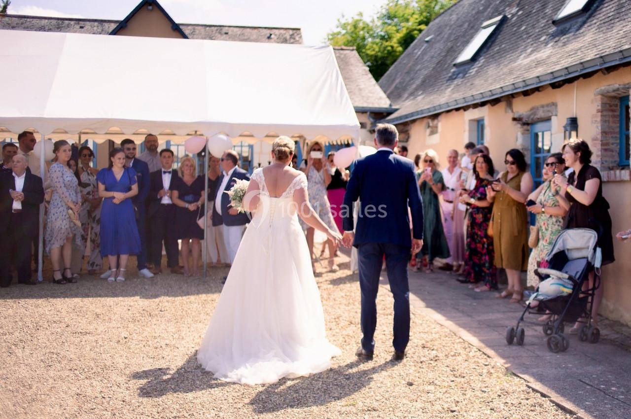 Un couple de mariés marche main dans la main vers des invités rassemblés devant une tente blanche.