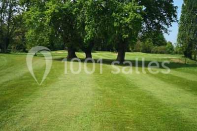 Salle à manger rustique avec table en bois dressée, mur en pierre apparente, étagères intégrées et cuisine ouverte.
