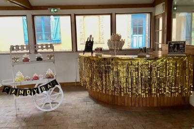 Salle à manger rustique avec table en bois dressée, mur en pierre apparente, étagères intégrées et cuisine ouverte.
