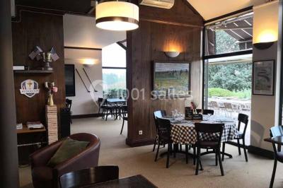 Salle à manger rustique avec table en bois dressée, mur en pierre apparente, étagères intégrées et cuisine ouverte.