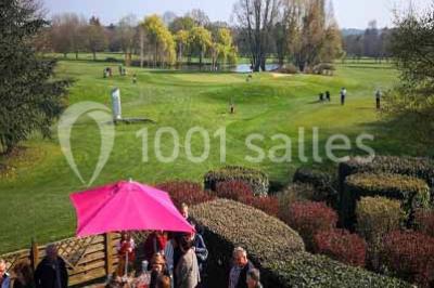 Salle à manger rustique avec table en bois dressée, mur en pierre apparente, étagères intégrées et cuisine ouverte.