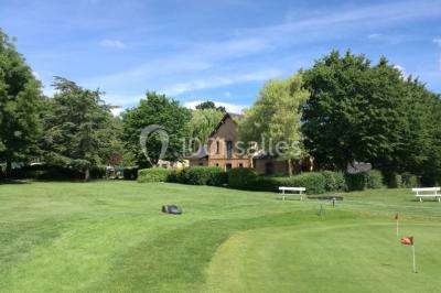 Salle à manger rustique avec table en bois dressée, mur en pierre apparente, étagères intégrées et cuisine ouverte.