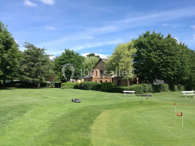 Pelouse bien entretenue avec un petit terrain de golf, entourée d'arbres et d'une maison en arrière-plan.