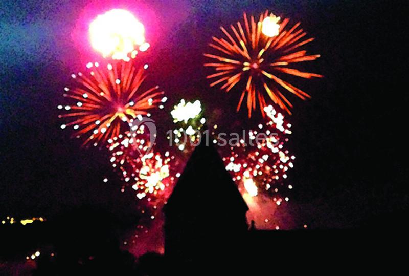 Feux d'artifice multicolores illuminant le ciel nocturne au-dessus d'une silhouette de bâtiment sombre.