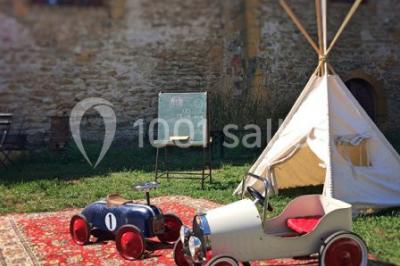 Deux voitures à pédales rétro sur un tapis rouge devant une tente tipi et un tableau noir dans un jardin.