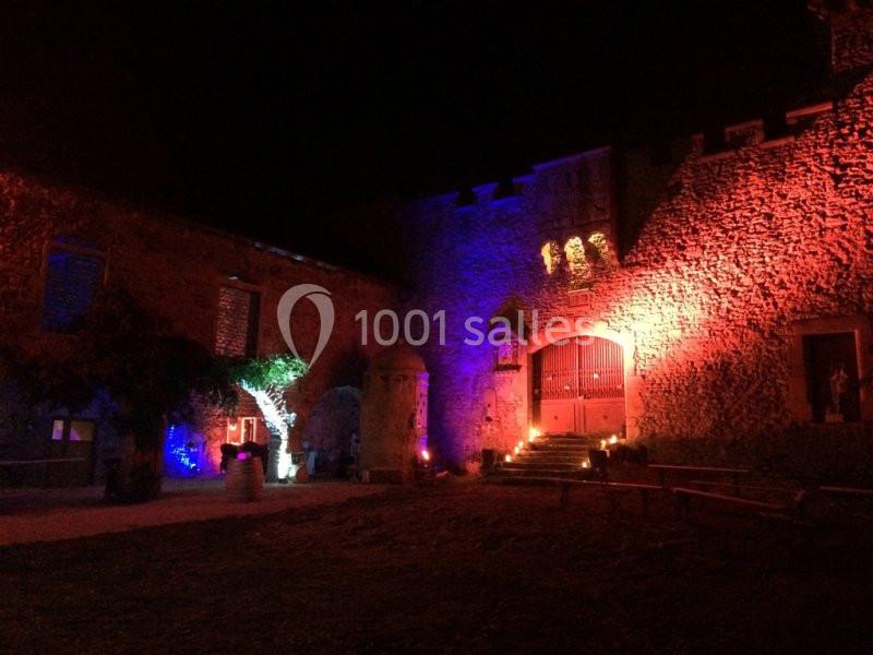 Façade d'un château illuminée de lumières colorées la nuit, avec des bougies disposées près de l'entrée.