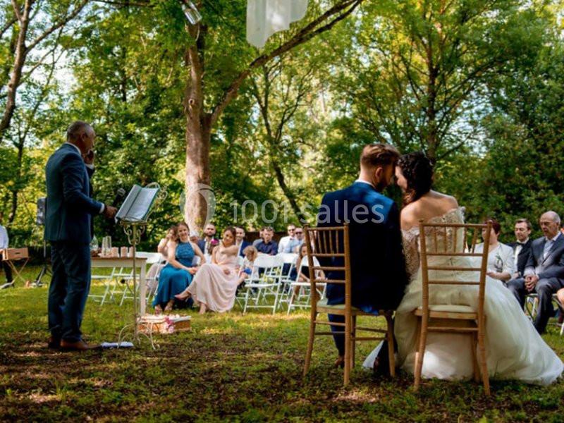 Un couple assis lors d'une cérémonie de mariage en plein air, entouré d'invités dans un cadre boisé.