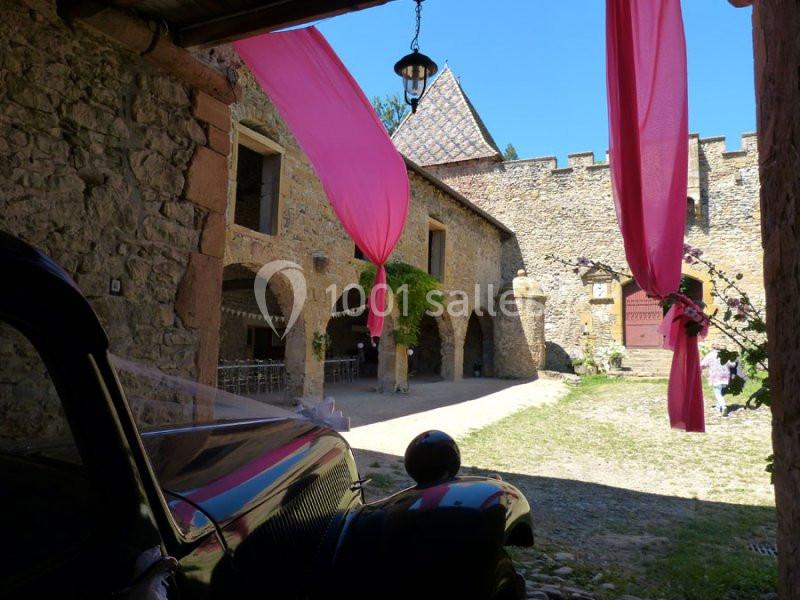 Vue d'une cour intérieure avec des murs en pierre, des drapés roses et une voiture ancienne au premier plan.