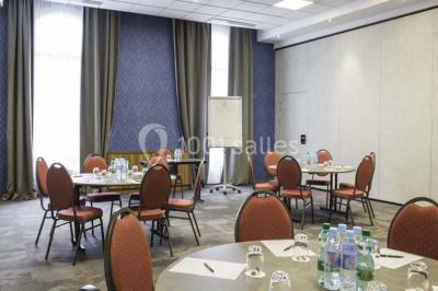 Chambre d'hôtel lumineuse avec lit double, coin salon, télévision murale et grandes fenêtres avec rideaux.