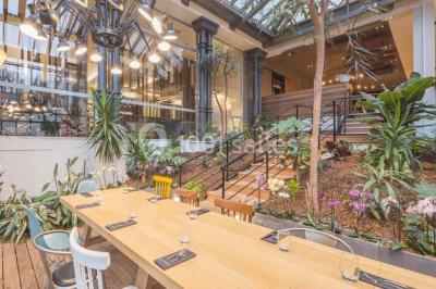 Chambre d'hôtel lumineuse avec lit double, coin salon, télévision murale et grandes fenêtres avec rideaux.