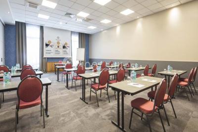 Chambre d'hôtel lumineuse avec lit double, coin salon, télévision murale et grandes fenêtres avec rideaux.