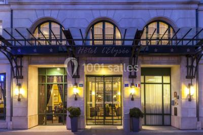 Chambre d'hôtel lumineuse avec lit double, coin salon, télévision murale et grandes fenêtres avec rideaux.