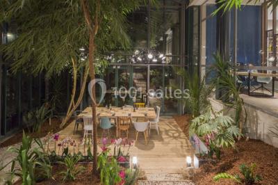 Chambre d'hôtel lumineuse avec lit double, coin salon, télévision murale et grandes fenêtres avec rideaux.