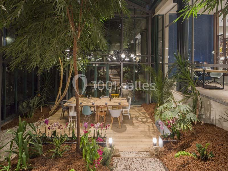 Salle à manger lumineuse entourée de plantes tropicales, avec une table en bois et des chaises colorées sur une terrasse en…