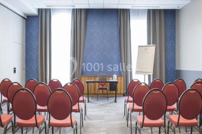 Chambre d'hôtel lumineuse avec lit double, coin salon, télévision murale et grandes fenêtres avec rideaux.