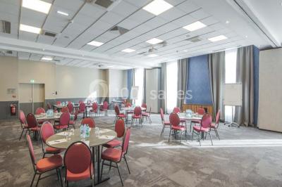 Chambre d'hôtel lumineuse avec lit double, coin salon, télévision murale et grandes fenêtres avec rideaux.