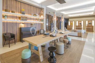 Chambre d'hôtel lumineuse avec lit double, coin salon, télévision murale et grandes fenêtres avec rideaux.