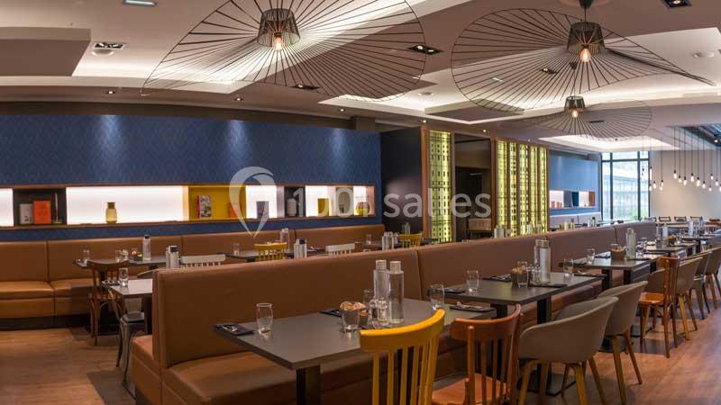 Salle de restaurant moderne avec tables dressées, banquettes en cuir, chaises variées et luminaires design suspendus.