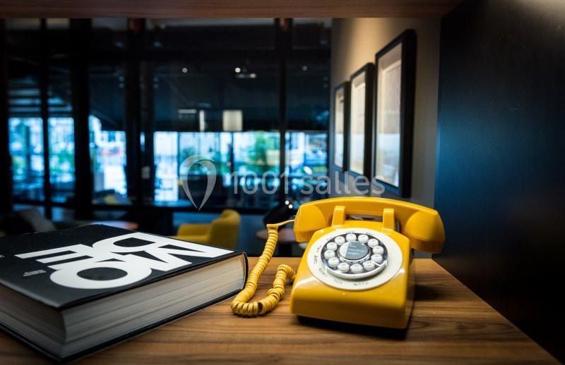 Téléphone fixe jaune rétro posé sur une table en bois, à côté d’un livre, dans un intérieur moderne et sombre.
