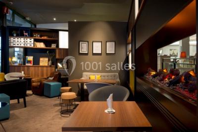 Chambre d'hôtel lumineuse avec lit double, coin salon, télévision murale et grandes fenêtres avec rideaux.