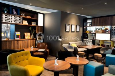 Chambre d'hôtel lumineuse avec lit double, coin salon, télévision murale et grandes fenêtres avec rideaux.