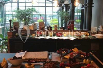 Chambre d'hôtel lumineuse avec lit double, coin salon, télévision murale et grandes fenêtres avec rideaux.