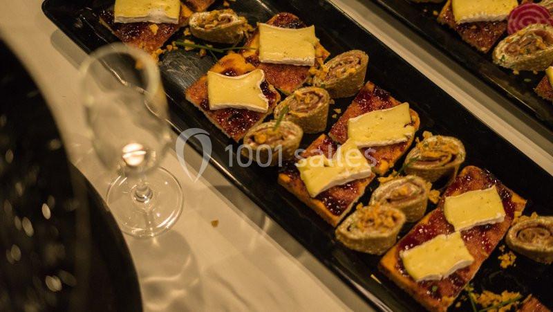 Plateau de toasts garnis de fromage, confiture et roulés apéritifs, posé sur une table avec une flûte vide.