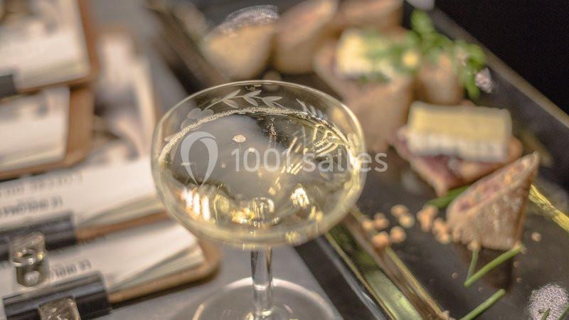 Verre de vin blanc pétillant sur une table avec des amuse-bouches et des couverts en arrière-plan.