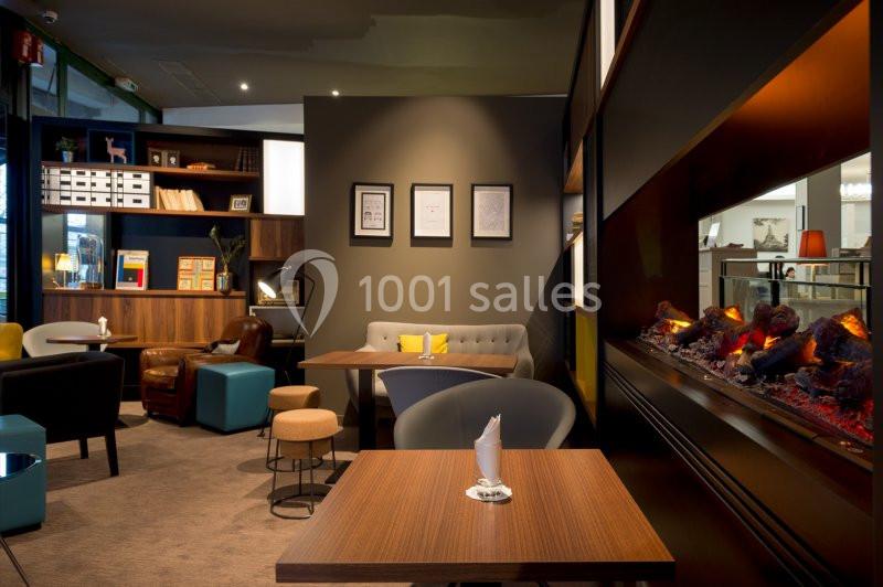 Espace intérieur chaleureux avec tables en bois, fauteuils confortables, étagères et cheminée électrique moderne.