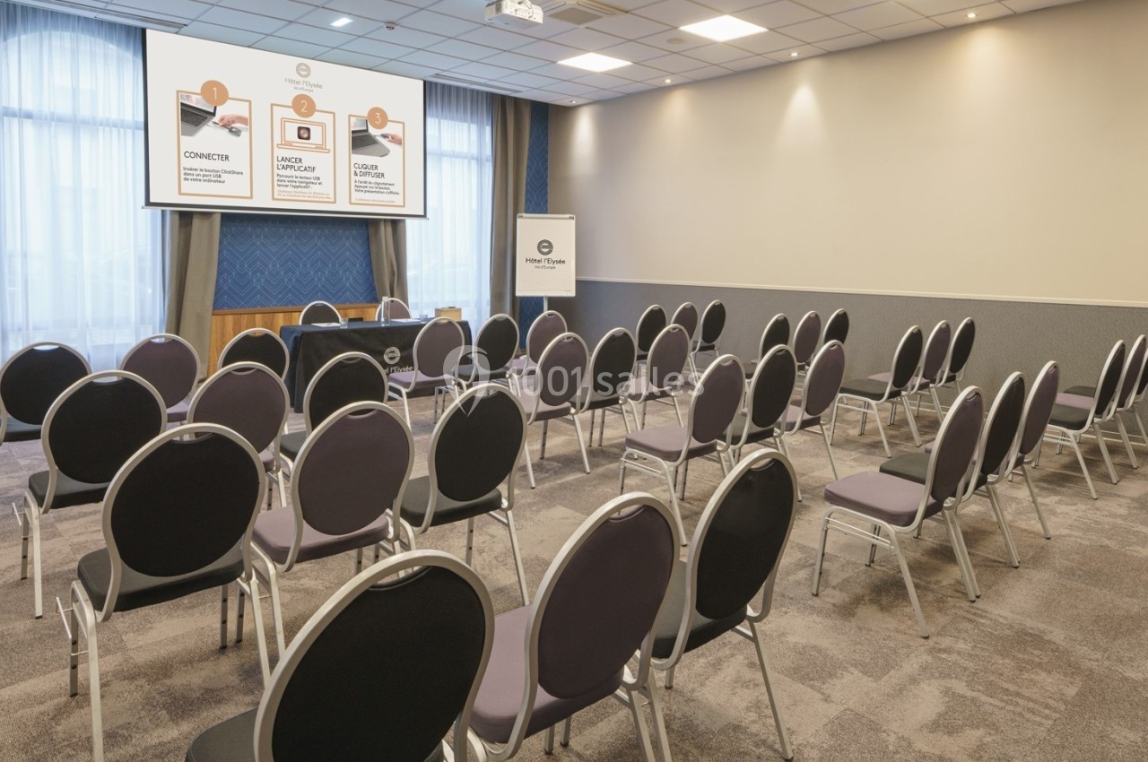 Salle de conférence avec des rangées de chaises vides, un écran de projection et un pupitre à l'avant.