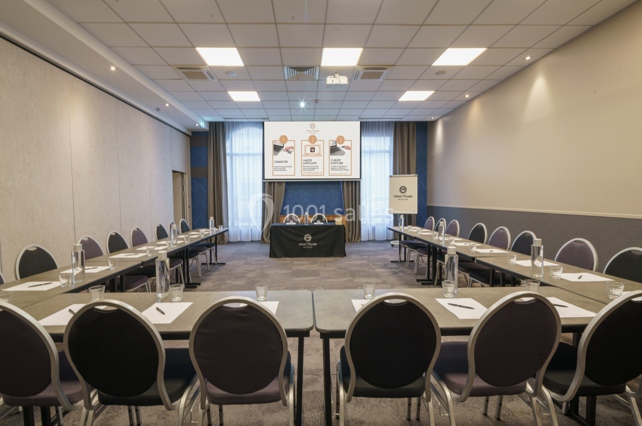 Salle de réunion lumineuse avec tables en U, chaises alignées, écran de présentation et matériel de conférence.