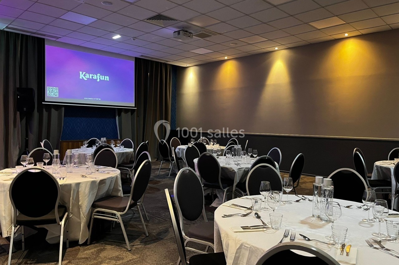 Salle de réception avec tables rondes dressées et écran de projection affichant ’Karafun’.