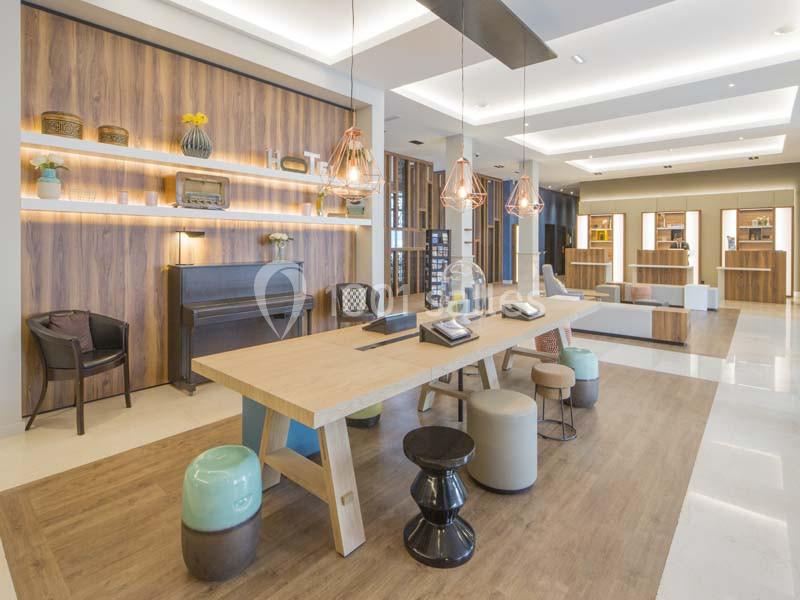 Espace intérieur moderne avec table en bois, tabourets variés, étagères décorées et éclairage suspendu.